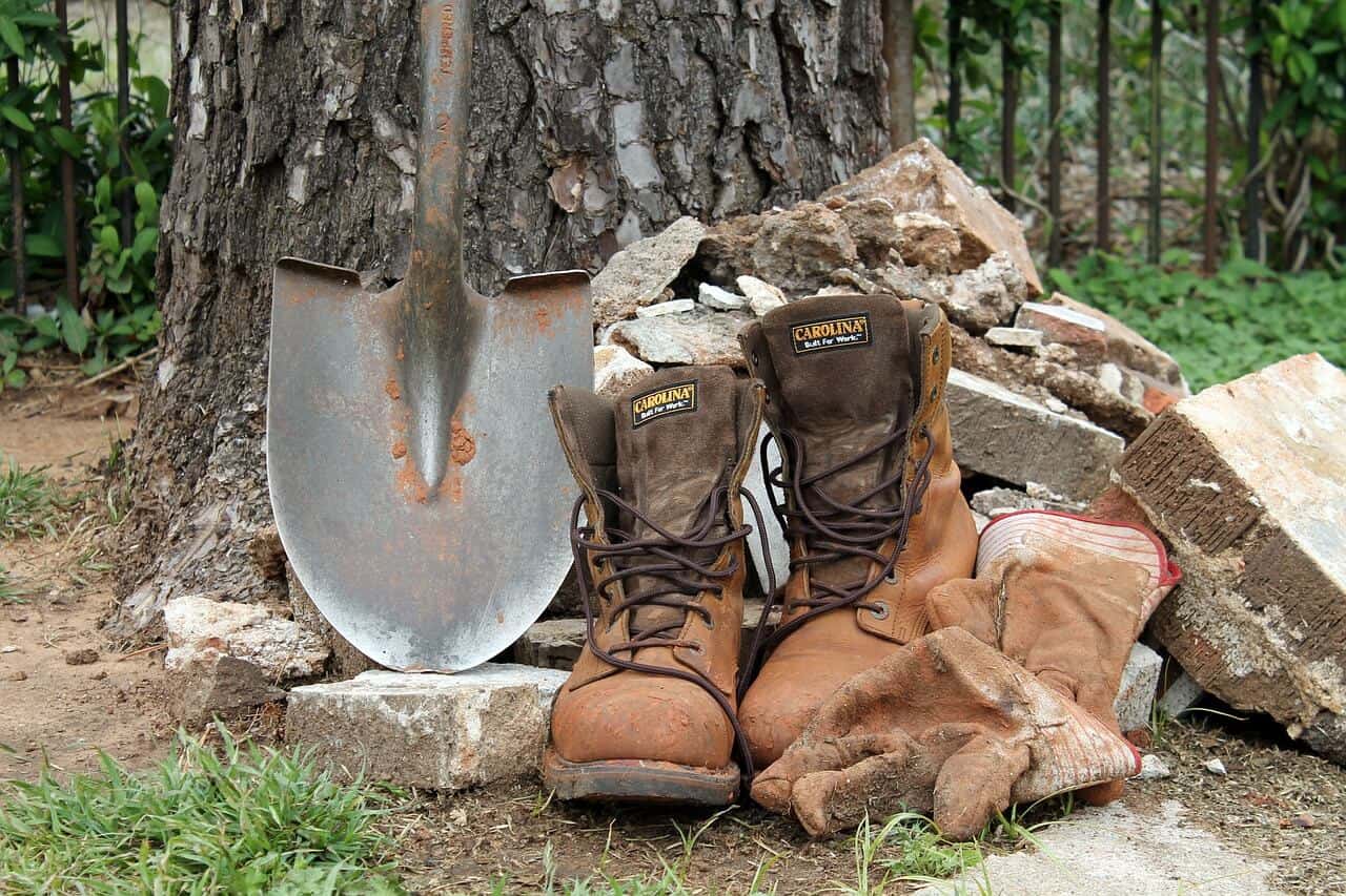 brown vegan work boots beside a tree, shovel and bricks