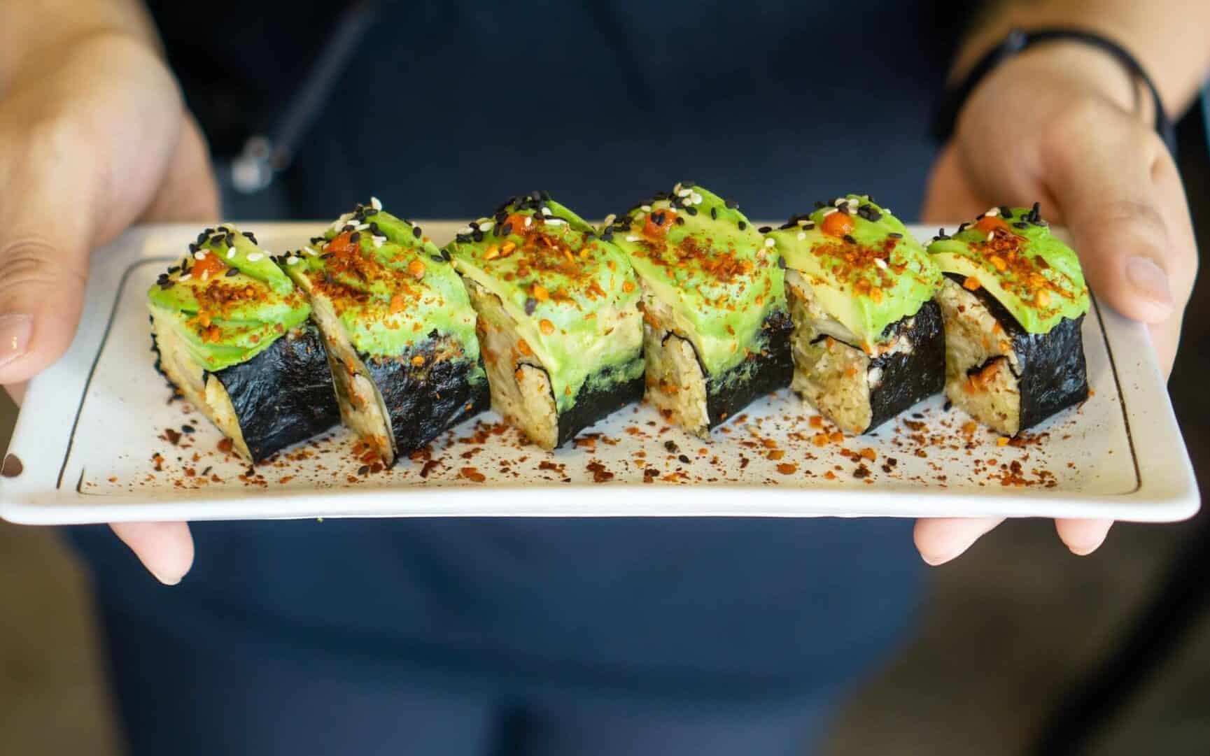 a person holding a plate with vegan avocado sushi pieces at vegan restaurants Newcastle